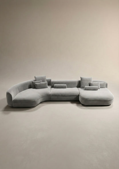 Large curved modular sofa in grey  velvet upholstery with sculptural form and modular layout