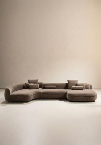 Large curved modular sofa in taupe velvet upholstery with sculptural form and modular layout
