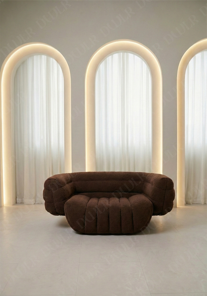 Brown curved sofa in a room with three arches and light curtains.