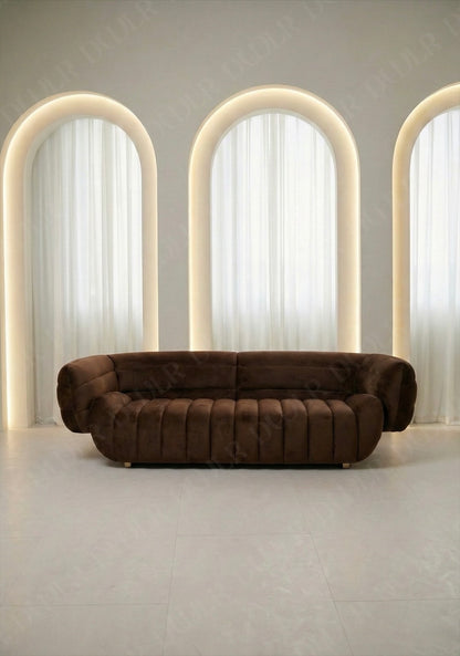 Solara sofa in brown velvet upholstery with curved silhouette and channel tufted seat in modern living room.