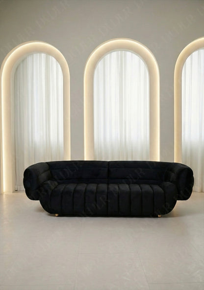 Solara sofa in black velvet upholstery with curved silhouette and channel tufted seat in modern living room.